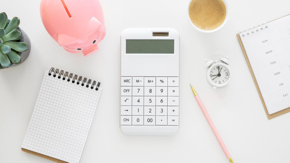 Mesa com calculadora, porquinho e blocos de anotações, representando gestão de dinheiro