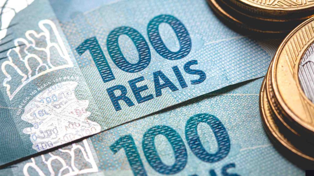 Moedas de um real sobrepostas a notas de cem reais