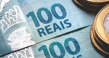 Moedas de um real sobrepostas a notas de cem reais